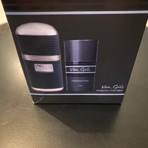 Van Gils Strictly for Men parfymset - Parfymset från Van Gils med en Eau de Toilette 50 ml och en Deodorant Stick 75 ml. Båda har en stilren svart design med silverdetaljer och märke på framsidan. Flaskan har räfflad yta och metallinslag, deodoranten är slät och svart med silvertext.