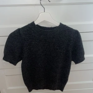 Mörkgrå stickad tröja med kort ärm - Säljer en mörkgrå stickad tröja med korta armar. Aldrig använd💕