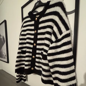 Randig kofta med guldknappar H&M - Säljer en fluffig svartvit randig kofta från ginatricot med snygga guldknappar framtill. Koftan har två fickor, rund halsringning och lång ärm.