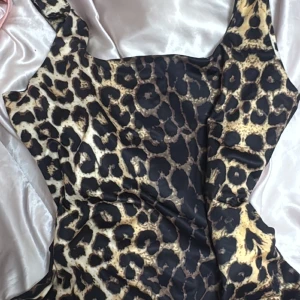 Leopardmönstrad kort topp - Säljer en snygg leopardmönstrad topp med breda axelband och fyrkantig urringning. Toppen  har en figurnära passform och är gjord i ett mjukt, glansigt material som känns lyxigt mot huden. Perfekt för dig som vill sticka ut med ett djuriskt print. Har knappt använt 