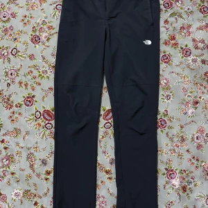 Svarta byxor från The North Face - Svarta byxor från The North Face med diskret logga på låret. Byxorna har raka ben, dragkedjeförsedda fickor och är tillverkade i ett slitstarkt syntetmaterial. Perfekta för dig som gillar outdoor och vill ha en clean look.