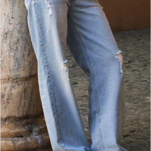 Ljusblå wide jeans med slitningar - Säljer ett par ljusblå jeans med breda ben och snygga slitningar på låren och knäna. Jeansen har klassisk femficksdesign, normal midja och är tillverkade i mjukt bomullsjeans. Perfekta för en avslappnad och trendig look.Nys med lapp kvar! Från Nelly