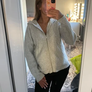 Ljusgrå ribbad hoodie med dragkedja - Mysig ljusgrå hoodie med ribbad struktur och dragkedja framtill. Tröjan har huva, långa ärmar och en relaxed passform. Perfekt för lager-på-lager och chill dagar.