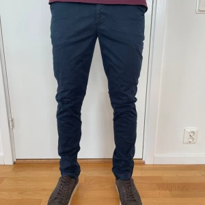 Mörkblå chinos från Tommy Hilfiger - Snygga mörkblå chinos från Tommy Hilfiger med klassisk passform och raka ben. Byxorna har sidfickor, bakfickor med knapp och är tillverkade i mjuk bomull. Perfekta för en clean och stilren outfit. Tveka inte att kontakta vid frågor.