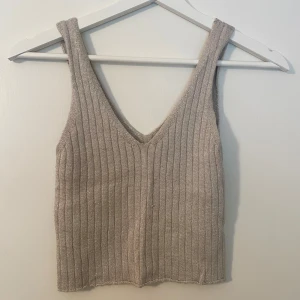 Vit/beige/silvrig ribbad stickad linnetopp - Säljer en vit/beige/silvrig stickad linnetopp med djup v-ringning och bredare axelband. Toppen är ribbstickad och har en croppad passform. Enkel att styla till jeans eller kjol. Toppen är i ”onesize” och materialet är stretchigt.