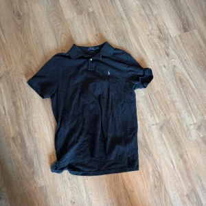 Ralph Lauren piké - Snygg svart/grå pikétröja från Polo Ralph Lauren i custom slim fit. Klassisk krage, korta ärmar och liten broderad logga på bröstet. Perfekt till jeans eller shorts för en clean och stilren look.