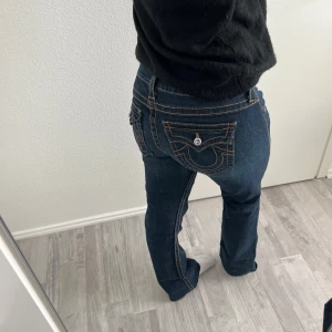 True Religion jeans - Säljer ett par ikoniska True Religion jeans i mörkblå denim med snygga fickdetaljer. Modellen är lågmidjad med bootcut-ben och klassiska knappar. Innerbebslägnd 30
