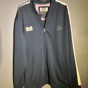 Weekend Offender tracksuit  - Mörkblå tracksuit från Weekend Offender med vita och rosa ränder längs sidorna. Byxorna har elastisk midja och dragsko vid benslut för extra komfort. Materialet är mjukt och stretchigt, perfekt för chill eller träning. Snygg logga broderad på benet. Denna tracksuit släpptes i ett limiterad antal och säljs inte längre. Köpt för 140€ och är i ny skick!!!