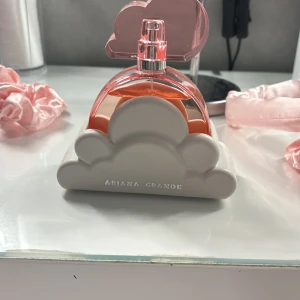 Ariana Grande Cloud parfym - Superfin parfym från Ariana Grande i modellen Cloud. Flaskan är rosa och formad som ett moln, med en vit molnformad bas i plast. Perfekt som en söt detalj på sminkbordet och doften är riktigt populär bland unga. 100 ml och endast lite använd 