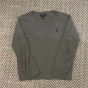 Grå stickad tröja från Polo Ralph Lauren - Snygg grå stickad tröja från Polo Ralph Lauren i storlek M i barn. Passar mellan 150-160cm lång ett litet hål därav de lite billigare priset. Om man har frågor eller funderingar är det bara att skriva!