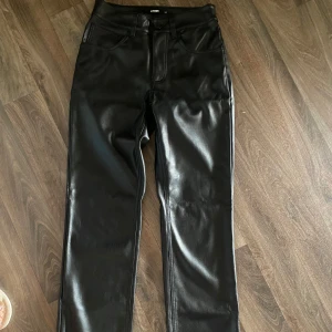 Svarta skinnbyxor från Bik Bok - Snygga svarta byxor i skinnimitation från Bik Bok. Low waist. De har raka ben, klassisk femficksdesign och normal passform. Perfekta för dig som vill ha en edgy look med lite glansig finish. Stängs med knapp och dragkedja framtill.