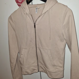 Beige hoodie med dragkedja  - Snygg beige hoodie  med dragkedja framtill, huva med snörning och två stora fickor. Perfekt för en chill och avslappnad stil. Långärmad och i mjuk bomull som känns skön mot huden.
