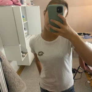 Vit t-shirt med leopardmönstrade läppar - Vit t-shirt från vila i storlek XS med korta ärmar och rund hals. På bröstet finns en cool leopardmönstrad läpp-detalj som gör den unik. T-shirten är gjord i mjuk bomull och har en normal passform. Perfekt för dig som gillar stilrena plagg med en twist.