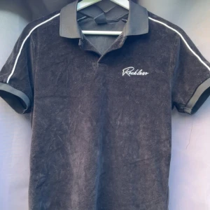 Svart Reckless t-shirt med krage - Svart t-shirt från Reckless med vit logga på bröstet och vita ränder längs axlarna. Klassisk pikékrage och korta ärmar. Materialet känns som mjuk bomull och passformen är normal. Priset kan diskuteras!