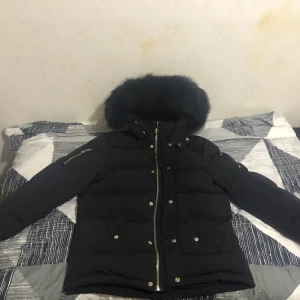 Svart Moose Knuckles dunjacka M - Säljer en svart dunjacka från Moose Knuckles med fluffig pälskant på huvan och snygga detaljer som dragkedjor och broderad logga. Jackan har lång ärm, flera fickor och coola metalldetaljer på ärmen. Perfekt för kalla dagar och riktigt street.