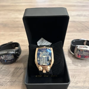 Futuristisk guldig klocka med synlig mekanik - Unik klocka med guldig boett och transparent urtavla som visar den coola mekaniken inuti. Klockan har svart armband och en modern, rektangulär form. Perfekt för dig som gillar teknik och vill sticka ut med en riktigt futuristisk accessoar.