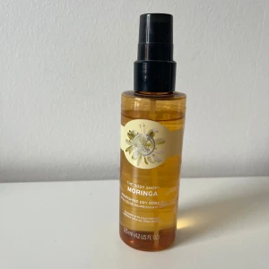The Body Shop Moringa Dry Body Oil - En närande torr kroppsolja med moringa från The Body Shop. Oljan kommer i en genomskinlig plastflaska med svart pump och rymmer 125 ml. Innehåller kallpressad moringafröolja från Rwanda och har en fräsch, blommig doft.