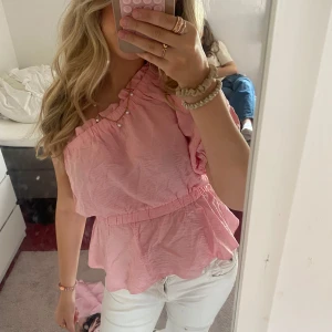 Rosa offshoulder volangtopp - Supersöt rosa topp med offshoulder och volangdetaljer. Den har en luftig och lätt känsla, resår i midjan och en asymmetrisk axel. Perfekt för dig som gillar en feminin och trendig stil.