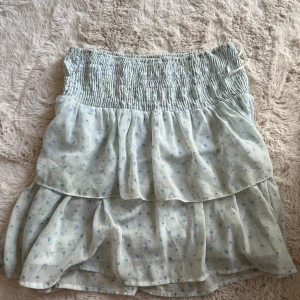 Ljusblå blommig volangkjol - Supersöt ljusblå kjol med små blommor och volanger. Kjolen har smock i midjan & väldigt stretchig. Inga tydliga tecken på användning, säljes då den är för stor - tvättas noga innan försäljning💘
