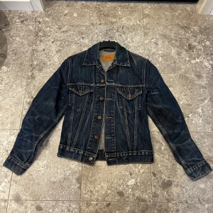 Levi's jeansjacka mörkblå S - Klassisk mörkblå jeansjacka från Levi's. Jackan har knappar framtill, två bröstfickor med lock och knapp samt snygg söm-detaljer. Perfekt för dig som gillar tidlös stil och vill ha en jacka som funkar året runt. Stl s med kort passform 