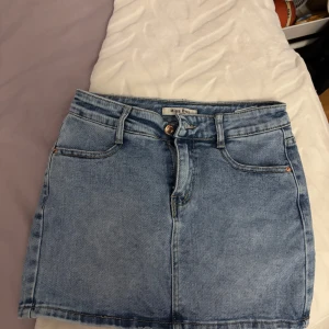 Ljusblå jeanskjol från Miss Bon - Snygg ljusblå jeanskjol från Miss Bon med dragkedja framtill. Perfekt för dig som gillar en enkel och stilren look. Kjolen är kort och passformen normal men ändå lite tajtare.