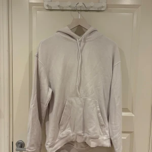 Vit hoodie med huva och magficka - En stilren vit hoodie med huva och snörning, samt en stor magficka framtill. Tröjan har en relaxed passform och är tillverkad i mjuk bomullsmix, perfekt för chill dagar eller när du vill ha en enkel och clean look.