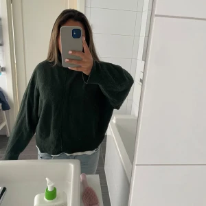 Mörkgrön stickad tröja med loose fit - Mysig mörkgrön stickad tröja med loose passform och långärmade ärmar. Tröjan har en enkel design med lite polokrage och är perfekt att slänga på över en t-shirt. Passar dig som gillar chill och oversized stil.