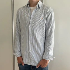 Blå vit Randig skjorta Polo Ralph Lauren  - Klassisk skjorta från Polo Ralph Lauren i vitt och ljusblått. Slim fit-modell och broderad logga på bröstet. Perfekt inför skolstarten🤩 skjortan är nästan helt ny och har inga fläckar eller defekter bara använd ungefär vid 3 tillfällen✅👍 Nypris: 1200kr mitt pris: 449kr om du har några funderingar så är det bara att skriva svarar alltid och priset är självklart inte hugget i sten🪨