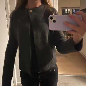 Mörkgrå kofta från Zara, S - En  mörkgrå kofta från Zara i storlek S. Koftan har rund halsringning, lång ärm och stängs med en enkel knapp upptill. Perfekt att slänga över en topp för en clean look. Materialet är mjukt och känns skönt mot huden.