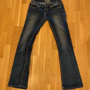 Lågmidjade bootcut jeans  - Snygga blå bootcut jeans från Rock & Roll med slitningar och kontrastsömmar. Låg midja och coola bakfickor med broderade detaljer. Jeansen har klassisk femficksdesign och är tillverkade i stretchig denim för skön passform.  Midjemått:35cm  innerbenslängden:82cm. Passar mig som är 173cm😊 storlek 26/34. Köpt hos en second hand för 650kr. priset går att diskutera!❤️