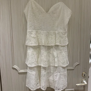 Vit spetsklänning från NLY Eve - Superfin vit kortklänning från NLY Eve med flera lager volanger och spetsdetaljer. Klänningen har smala axelband, v-ringad urringning och dragkedja i ryggen. Perfekt för dig som vill ha en romantisk och feminin look.