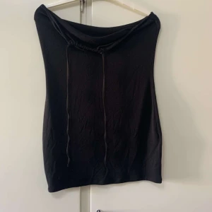 Svart väst med snörning i halsen - En stilren svart väst med dragsko och snörning vid halsen. Västen har en enkel, rak passform och är tillverkad i ett mjukt material som känns skönt mot huden. Perfekt att slänga över en t-shirt eller långärmad tröja för en cool look.