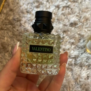 Valentino parfym 30ml nitat flaska - Snygg parfym från Valentino i en 30ml flaska. Flaskan är fyrkantig med nitar och mönstrad glasstruktur, svart kork med coola detaljer och etikett med grön text. Innehållet är ljusgult. Perfekt för dig som gillar lyxiga och unika dofter.