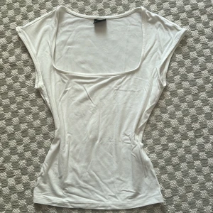 Vit croppad topp med fyrkantig hals - Säljer en vit croppad topp från Gina Tricot i storlek XS. Toppen har en snygg fyrkantig halsringning och är ärmlös med breda axelpartier. Materialet är mjukt och stretchigt, perfekt för en chill och stilren look. Passar dig som gillar minimalistisk stil.