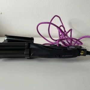 Svart vågtång från HH Simonsen - Säljer en svart vågtång från HH Simonsen med lila sladd. Perfekt för att skapa snygga beach waves och volym i håret. Ergonomiskt handtag och breda plattor i metall för enkel styling. Sladden är lång och flexibel för smidig användning.