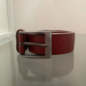 Brunt skärp i läder från Replay - Snyggt brunt bälte från Replay i läder med klassiskt silverfärgat spänne där Replay-loggan är ingraverad. Bältet är stilrent och har en rak, bred design utan mönster. Perfekt för att lyfta din outfit med en touch av färg.