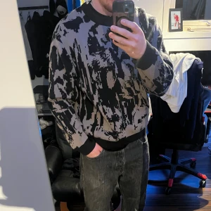 Svart och grå mönstrad stickad tröja från weekday  - Säljer en stickad tröja med abstrakt svart och grått mönster. Tröjan har rund halsringning, långa ärmar och ribbade muddar vid ärmslut och nederkant. Perfekt för dig som gillar en unik och modern stil. Inte använd mycket alls så är som i nyskick, tjockare material så väldigt varm, skön och rejäl!