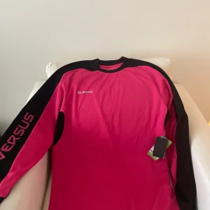 Rosa långärmad träningströja från SOC - Säljer en rosa långärmad träningströja från SOC i storlek M. Tröjan har svarta detaljer längs ärmarna och vadderade partier på armbågarna. Tillverkad i snabbtorkande syntetmaterial, perfekt för sport och aktivitet.