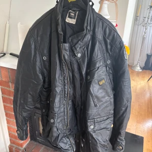 Svart jacka från G-Star RAW - Säljer en svart jacka från G-Star RAW med flera fickor och detaljer som dragkedja och knappar. Jackan har hög krage och en cool, lite robust look. Perfekt för dig som gillar streetwear och vill ha något som sticker ut.