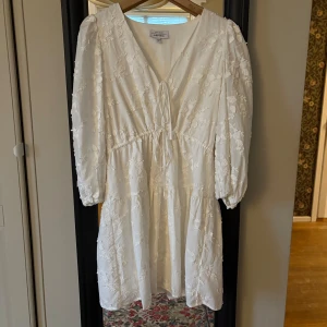 Vit blommig klänning med knyt och puffärm från By Malina - Säljer min superfina student klänning från & other stories med broderade blommor, v-ringning och knyt framtill. Klänningen har puffiga långa ärmar och är i kort modell. Perfekt som student klänning, och bara använd en gång!