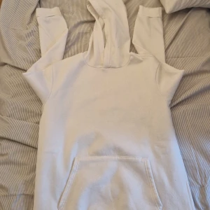 Vit hoodie med tryck 'Fashion Rebirth' - Säljer en vit hoodie med huva och magficka. På ryggen finns ett stort svart tryck med texten 'FASHION REBIRTH' och mindre text under. Perfekt för en avslappnad och trendig stil.