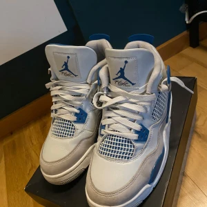 Nike Air Jordan 4 Retro White/Blue - Säljer ett par Nike Air Jordan 4 Retro i vitt och blått. Skorna har klassisk meshpanel, blå detaljer och Jumpman-logga på plösen. Perfekta sneakers för dig som gillar streetwear och vill sticka ut med en ikonisk modell.
