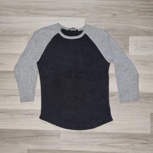 Svart och grå långärmad tröja - Säljer en stilren långärmad tröja med svart kropp och ljusgrå ärmar. Tröjan har rund halsringning och klassisk baseboll-look. Perfekt för en avslappnad stil.