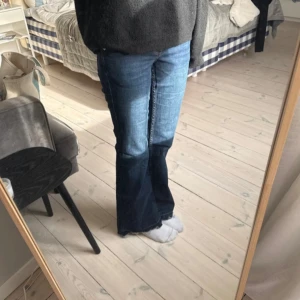 Blå bootcut jeans med broderad bakficka - Säljer ett par klassiska blå bootcut jeans med snygg broderad detalj på bakfickan. Jeansen har normal passform och stängs med knapp och dragkedja. Perfekta till vardags och lätta att matcha med olika toppar.