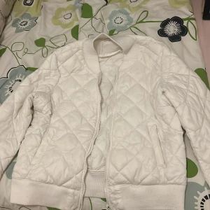 Vit bomberjacka - Säljer en vit bomberjacka med dragkedja framtill och ribbade muddar vid ärmslut och midja. Jackan har en klassisk bombermodell och är perfekt för dig som vill ha en stilren och enkel look.☺️
