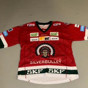 Röd Frölunda Indians hockeytröja - Säljer en röd hockeytröja från Frölunda Indians med gröna och vita detaljer. Tröjan har klubbens l framtill, flera sponsormärken och är signerad av spelare. En riktig unik tröja från 2021 limited edition original DM vid intresse och pris 