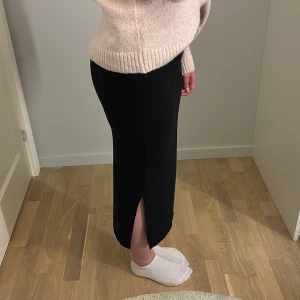 Svart ribbad kjol  - Svart långkjol från Pieces i ribbat material. Kjolen har en slits på ena sidan och är i storlek xs. 