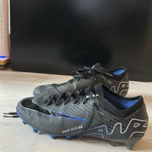 Nike Mercurial Elite fotbollsskor i svart och blå - Säljer ett par Elite Nike Mercurial fotbollsskor i svart och blå. Det är konstgräs+gräsdobbning, de funkar alltså för båda. Perfekta för dig som vill ha lätta och snabba skor på planen. Nypris: 2900kr Storlek: 42.5 men passar både större och mindre!