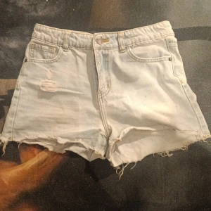 Ljusblå jeansshorts från UNIQ - Ljusblå jeansshorts från UNIQ med fransig kant och slitningar framtill. Klassisk femficksmodell med knapp och dragkedja. Perfekta för varma dagar och enkel att matcha med olika toppar.