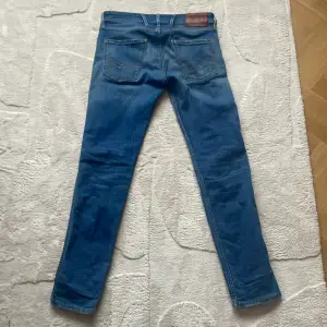 Säljer ett par klassiska blå jeans från Replay med raka ben och fem fickor. Byxorna har snygga slitningar och detaljerade sömmar på bakfickorna. Märkespatch i läder baktill i midjan och Replay-logga på fickan fram.
